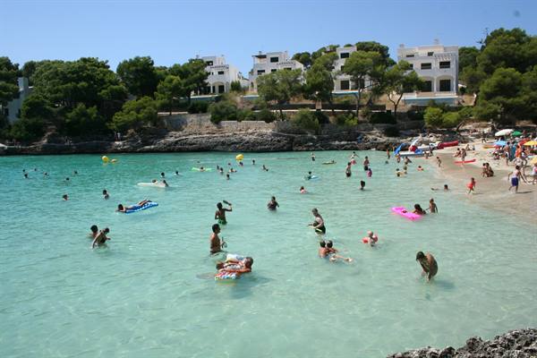 Bathers floating on inflatables in a sandy cove, white houses among pines