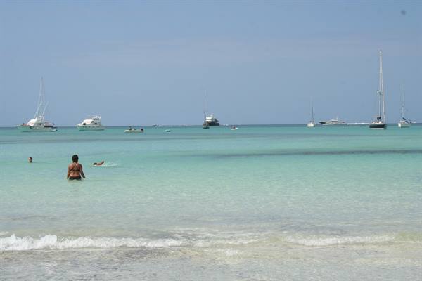 Swimmers in turquoise water with yachts and sailboats on the horizon