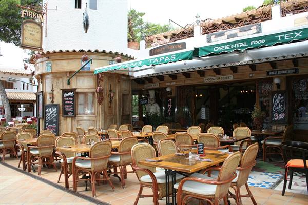 Empty wicker tables outside the Firkin bar under green awnings