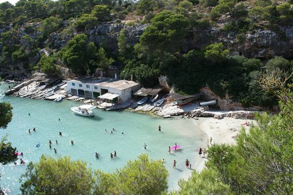 Swimmers in turquoise water beside a wooden hut and wooded cliffs