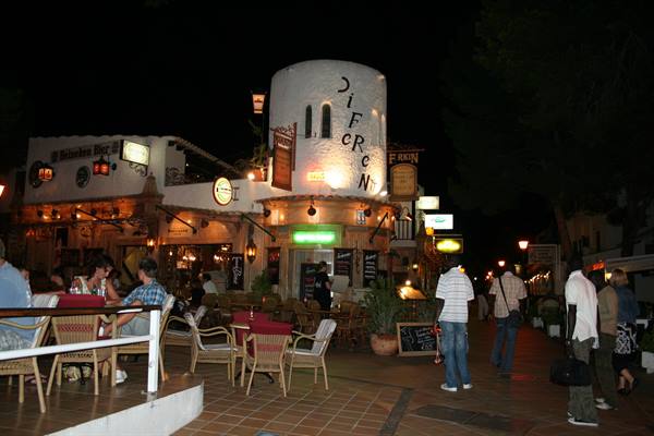 Citron bar lit at night, outdoor wicker tables and people strolling past