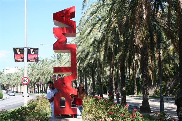 Tourists beside the big red Palma sign among palms and flowers