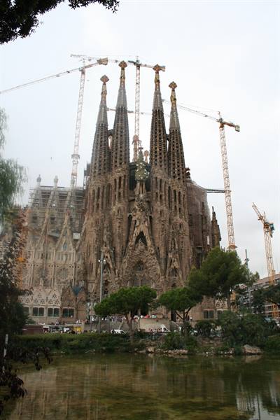 Sagrada Familia in Barcelona, stone towers with cranes and pond in front