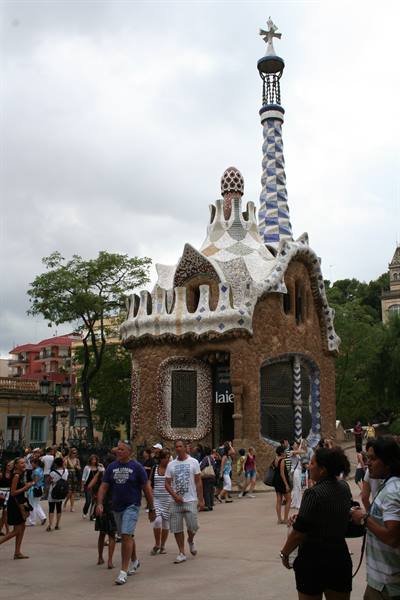 Tourists by Gaudí's mosaic lodge with spire, Park Güell, overcast sky