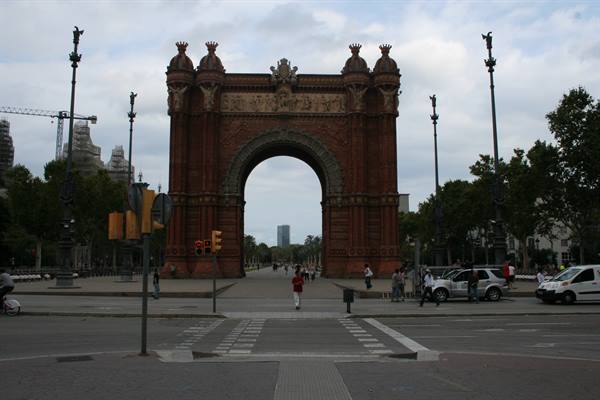 Red brick Arc de Triomf in Barcelona, pedestrians crossing the street under cloudy sky