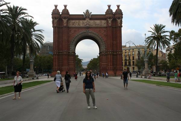 Tourist posing in front of Barcelona's Arc de Triomf, red bricks and palm trees