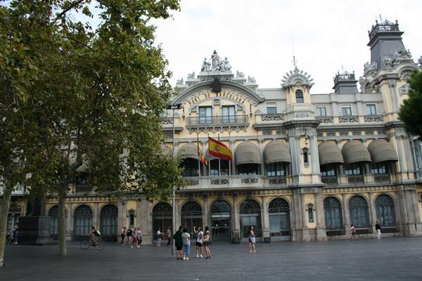Tourists in front of the modernist Port de Barcelona building, Spanish flag