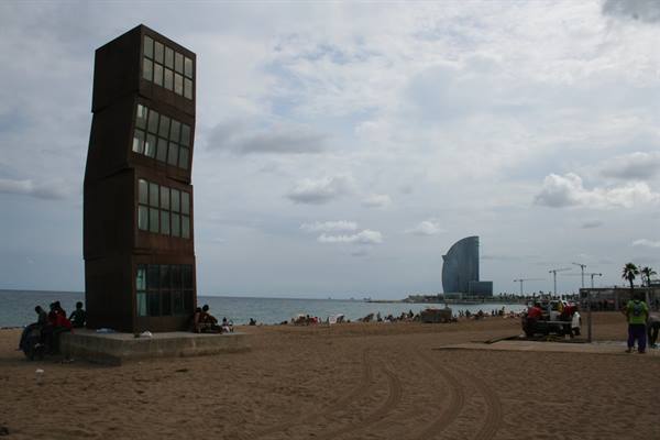 Corten steel sculpture on Barceloneta beach, sail-shaped hotel in the background