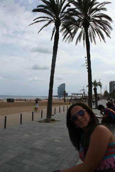 Girl in sunglasses beneath Barceloneta palms, with the beach and sail tower