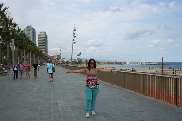 Woman with arms outstretched on Barceloneta boardwalk among palms and skyscrapers