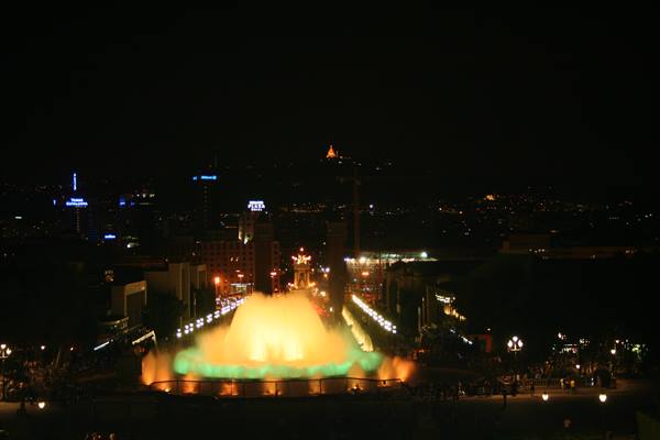 Magic Fountain of Montjuïc glowing yellow and green at night with city lights