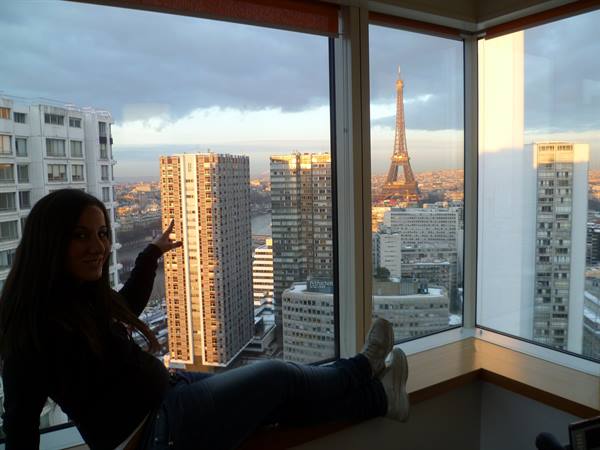 Girl on windowsill pointing at the Eiffel Tower among Paris skyscrapers