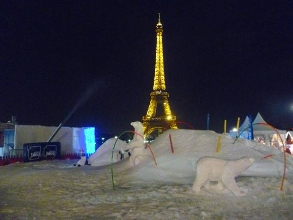 Polar bear snow sculptures in front of the illuminated Eiffel Tower at night