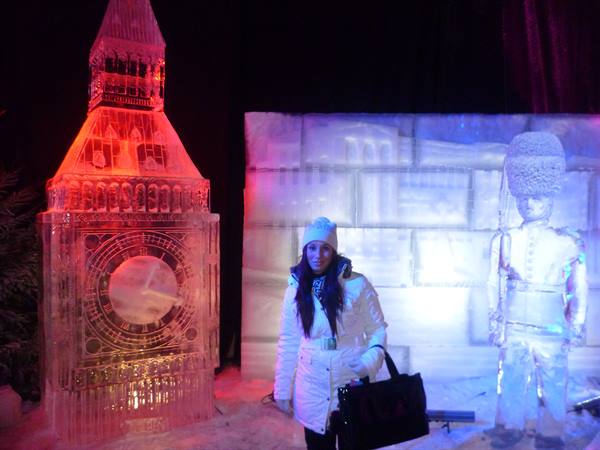 Woman beside ice sculptures of Big Ben and a royal guard, lit up