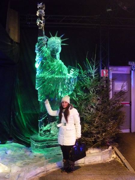 Woman posing next to an ice sculpture of the Statue of Liberty lit in green