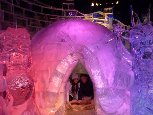 Couple inside a carved ice igloo lit by pink and purple lights