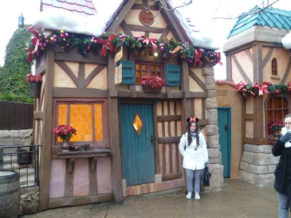 Girl with Minnie ears in front of a half-timbered wooden cottage decorated for Christmas, Disneyland
