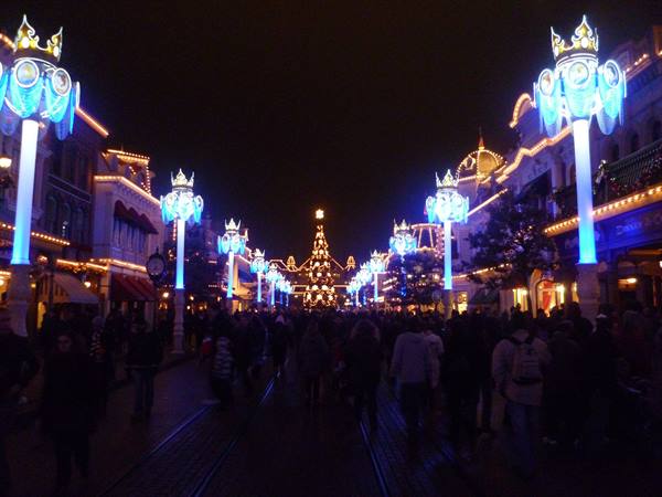 Avenue with blue lights and Christmas garlands, crowd at night, Disneyland