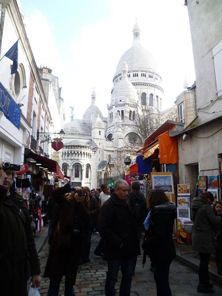 Crowded sloping street in Montmartre with the white dome of Sacré-Cœur