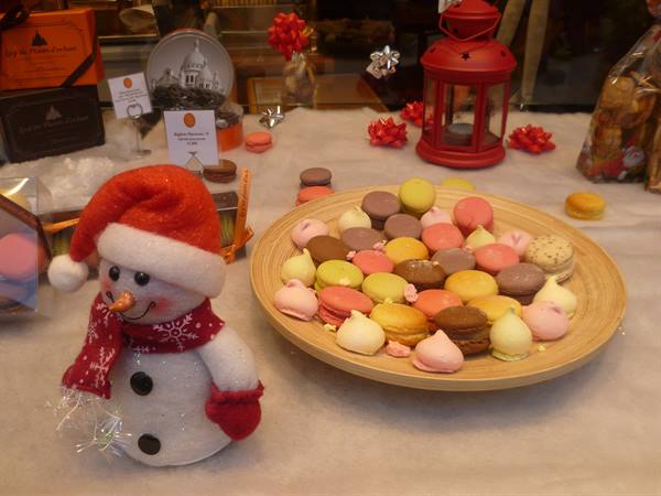 Fabric snowman in red hat beside a wooden plate of colorful macarons