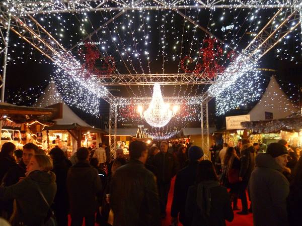 Crowded Christmas market under a chandelier of lights and metal trusses