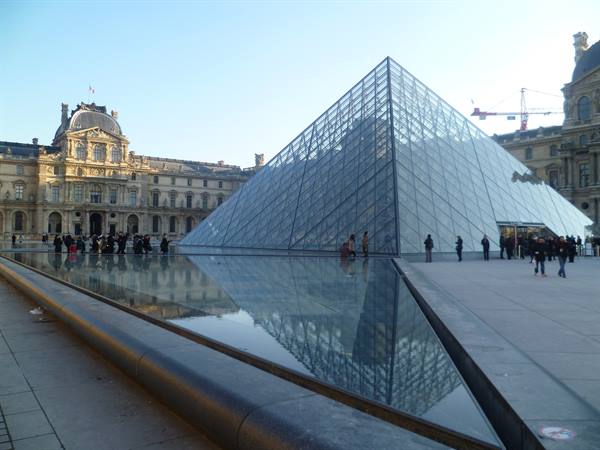 Louvre glass pyramid reflected in the pool, visitors under clear sky