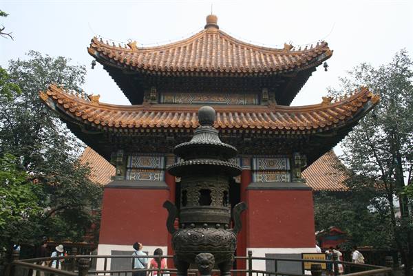 Buddhist temple with golden tiled roofs and large bronze incense burner, visitors below