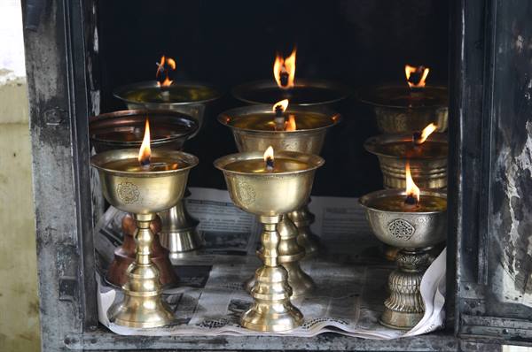 Brass butter lamps burning inside a Buddhist shrine niche