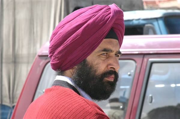 Sikh man wearing magenta turban and long beard beside a red van