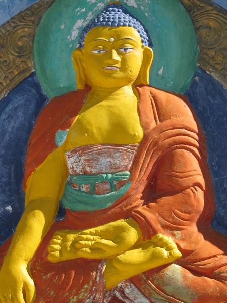 Painted Buddha statue in yellow and orange robes, blue halo, sunlight