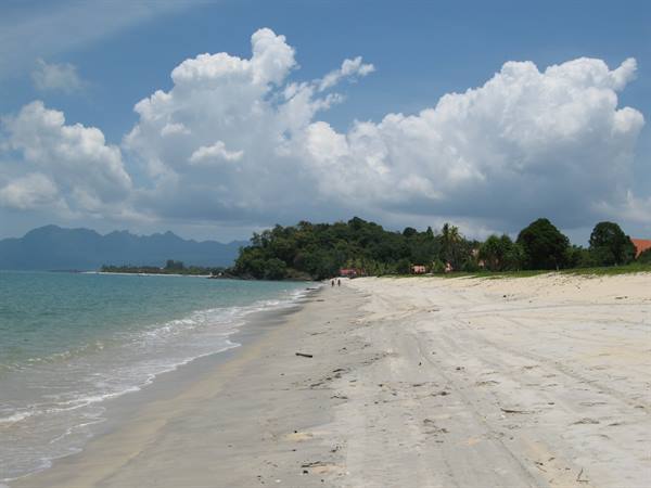 Pale sandy beach with gentle waves, green hill and white clouds