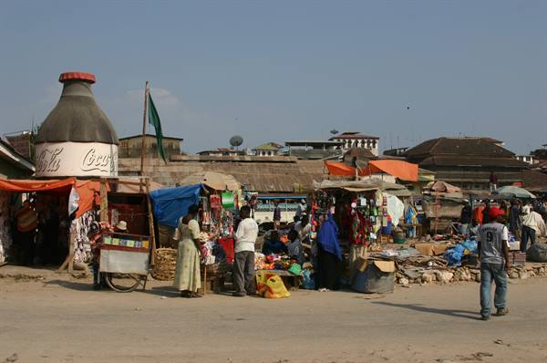 Street market with colorful stalls and vendors under a giant Coca-Cola bottle
