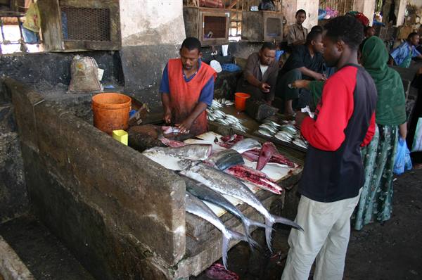 Fishmonger cutting tuna on stone slab at fish market, customers watching