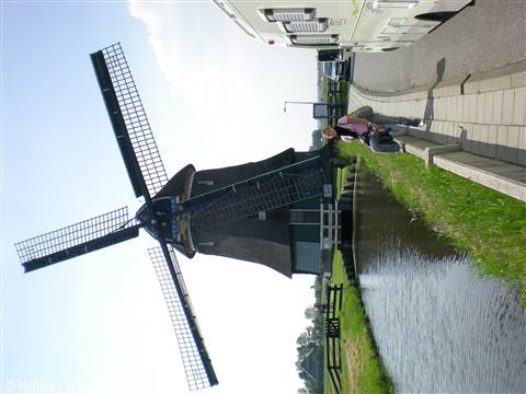 Wooden windmill beside a canal, person with parked camper van
