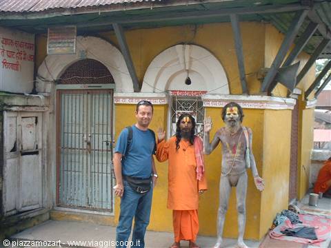 Tourist beside two ash-covered sadhus in front of a yellow temple