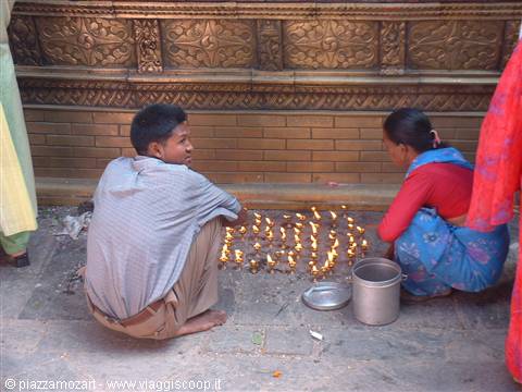 Man and woman crouching light small oil lamps at a carved temple wall