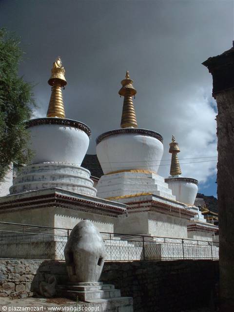 Three white stupas with golden spires under a cloudy sky