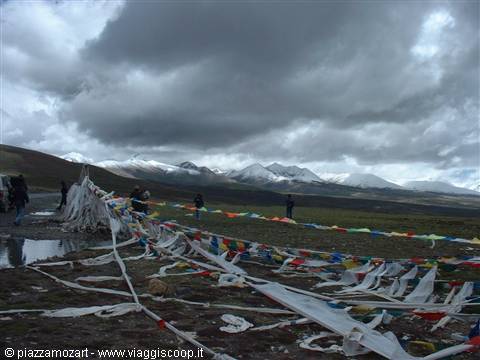 Tibetan prayer flags at a mountain pass under dark storm clouds