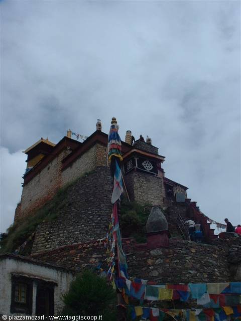 Ancient Tibetan stone monastery with colorful prayer flags under cloudy sky