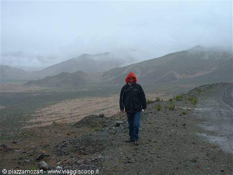 Walker in red hooded jacket on gravel road among foggy hills