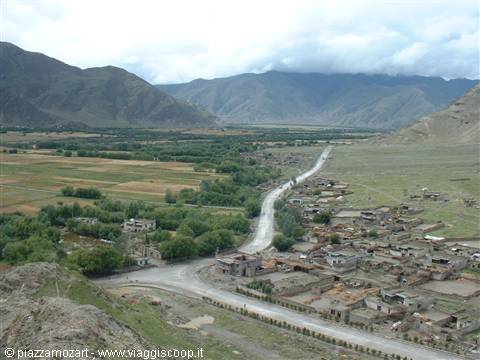 Road crossing a brick village among cultivated fields and cloudy mountains