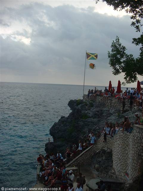 Crowd on dark stone terraces above the sea, Jamaican flag waving