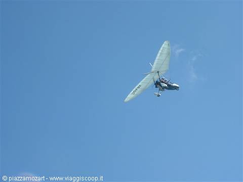 White microlight aircraft flying in blue sky with pilot aboard