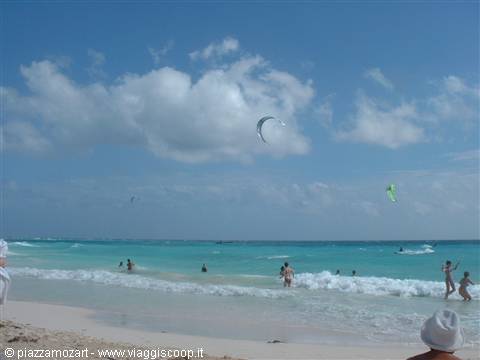 Bathers in turquoise Caribbean water, kitesurfing kite under cloudy sky