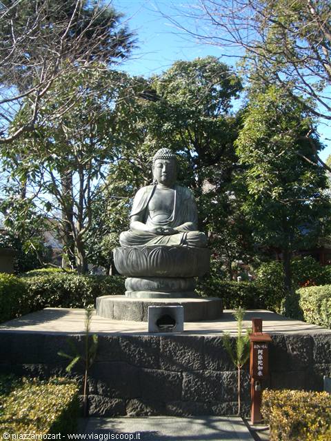 Bronze Buddha statue seated on lotus flower, trees and blue sky