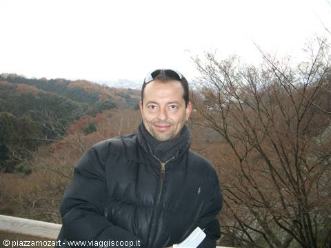 Man in black down jacket and sunglasses among bare autumn trees
