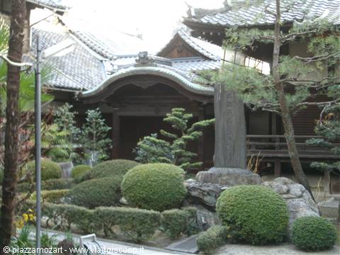 Japanese temple with curved tiled roofs, trimmed shrubs and stone stele