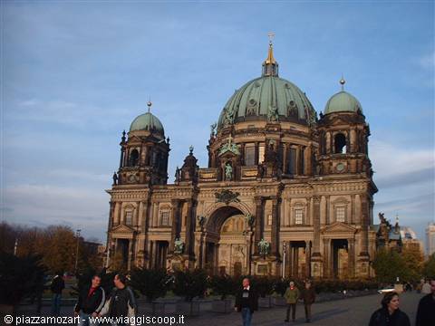 Tourists walk in front of Berlin Cathedral's stone facade under blue sky