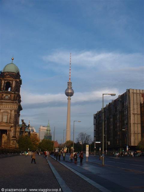 Berlin's Fernsehturm towers over Karl-Liebknecht-Straße, pedestrians under a cloudy sky