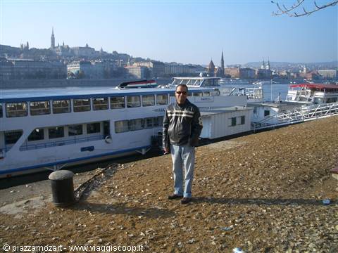 Man in leather jacket on the Danube riverbank, white boats moored, Budapest skyline behind